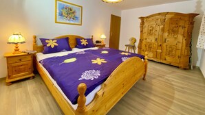 Een slaapkamer met een houten bed, paars beddengoed, een houten kledingkast en twee nachtlampjes.