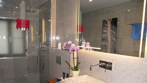 Een moderne badkamer met een douche in glazen cabine, een houten wastafelmeubel met een marmeren wastafel en een grote spiegel.
