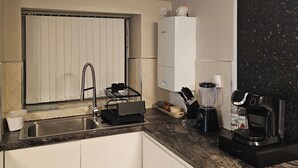 Een kleine keuken met een spoelbak, een ingebouwde oven, een koffiezetapparaat en een blender op het aanrecht.