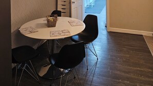Een eetruimte met een ronde tafel, zwarte stoelen, een klok en een deur naar een andere kamer.