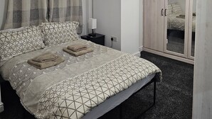 Een slaapkamer met een bed, nachtkastje, garderobe en spiegel.