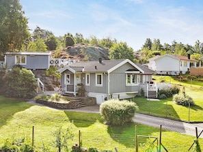 A row of small, single-story houses with a uniform architectural style, surrounded by well-maintained lawns and a rocky hillside in the background. - 4 Star Holiday Home in Svanesund (Svanesund)