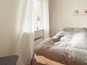 Une chambre à coucher avec un lit, une table de chevet, une lampe et une fenêtre avec des rideaux.