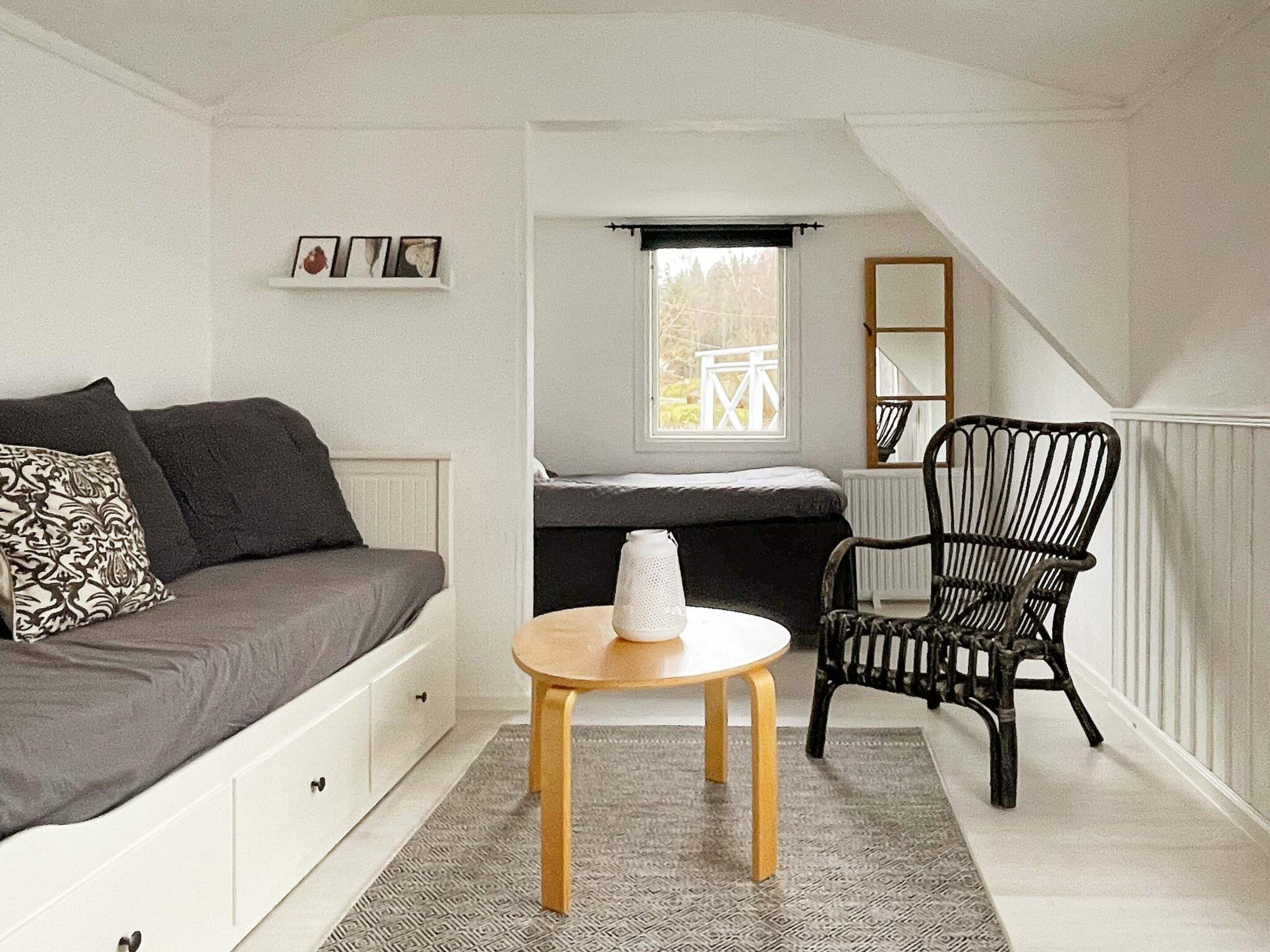 A compact room with a sofa, a small table with a tissue box, a chair, a window with a view, and a mirror on the wall.