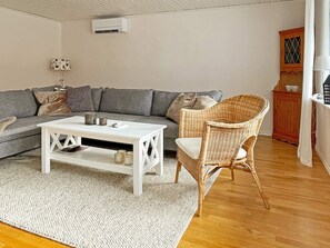 Een woonkamer met een grijze bank, een witte salontafel, een rieten stoel, een wit tapijt en een houten kast.
