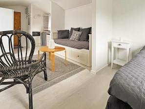 Ein gemütlicher, kompakter Wohnraum mit einer Couch, einem kleinen Tisch, einem Sessel und einem Nachttisch.