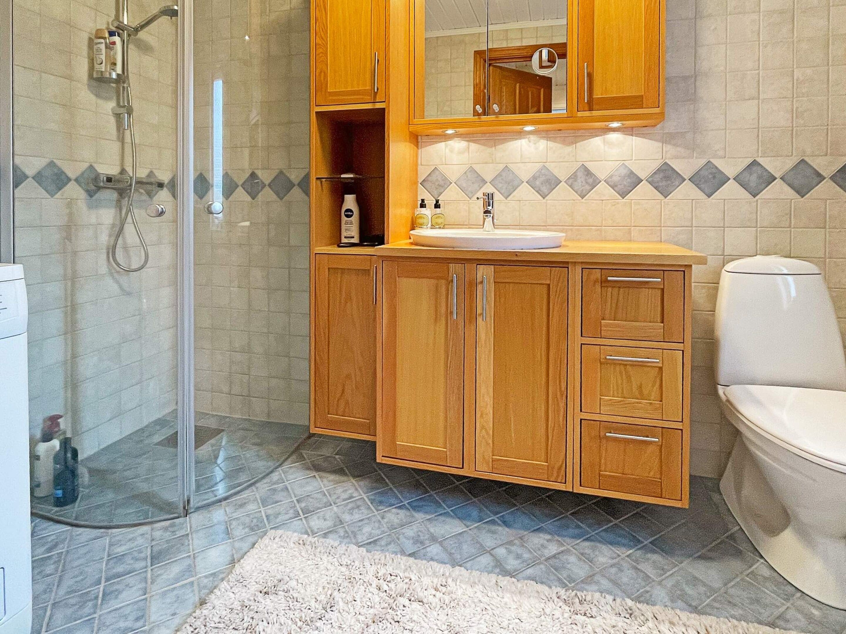 Un baño con cabina de ducha de vidrio, armarios de madera, un lavamanos blanco y un inodoro.