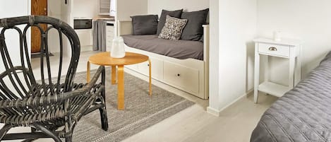 A compact bedroom with a single bed, a small bedside table, a chair, and a sofa bed.
