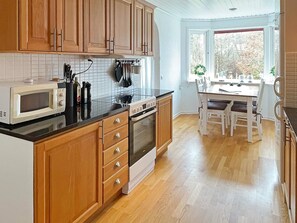 Une cuisine dotée de meubles en bois, d’un four à micro-ondes, d’un four traditionnel et d’un coin repas avec une table et des chaises.