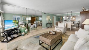 A spacious living room with a large TV, comfortable seating, a dining area, and a kitchen. - 30-Foot Oceanfront Balcony |Oceanfront Pool|Heart of Destin (Destin)