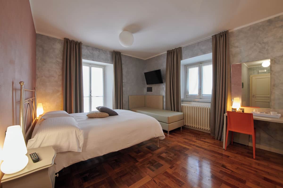 A hotel room with a bed, a desk, a chair, a TV, and a window.