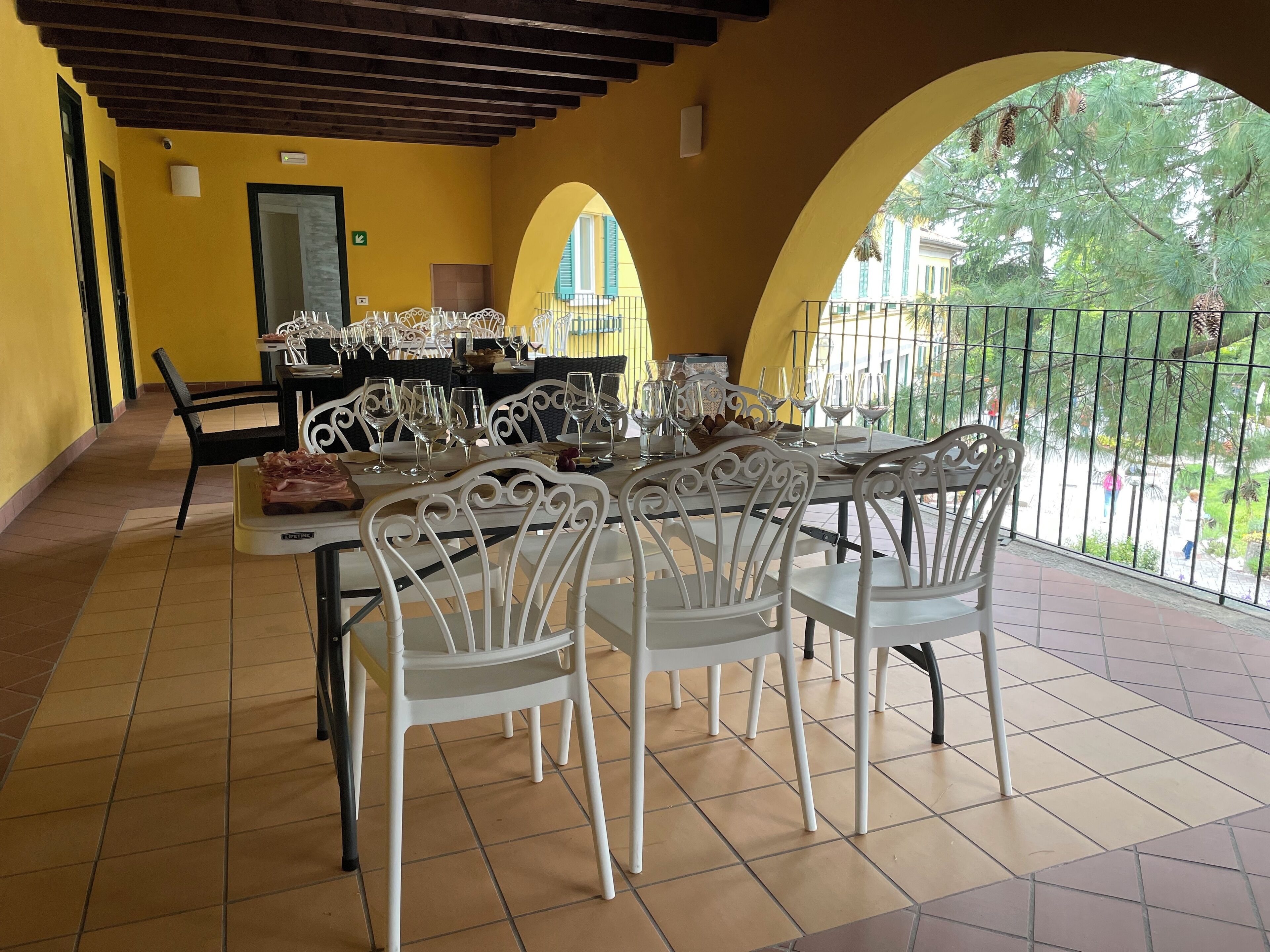 A dining area with white chairs and tables, yellow walls, and a view through an archway to the outside.