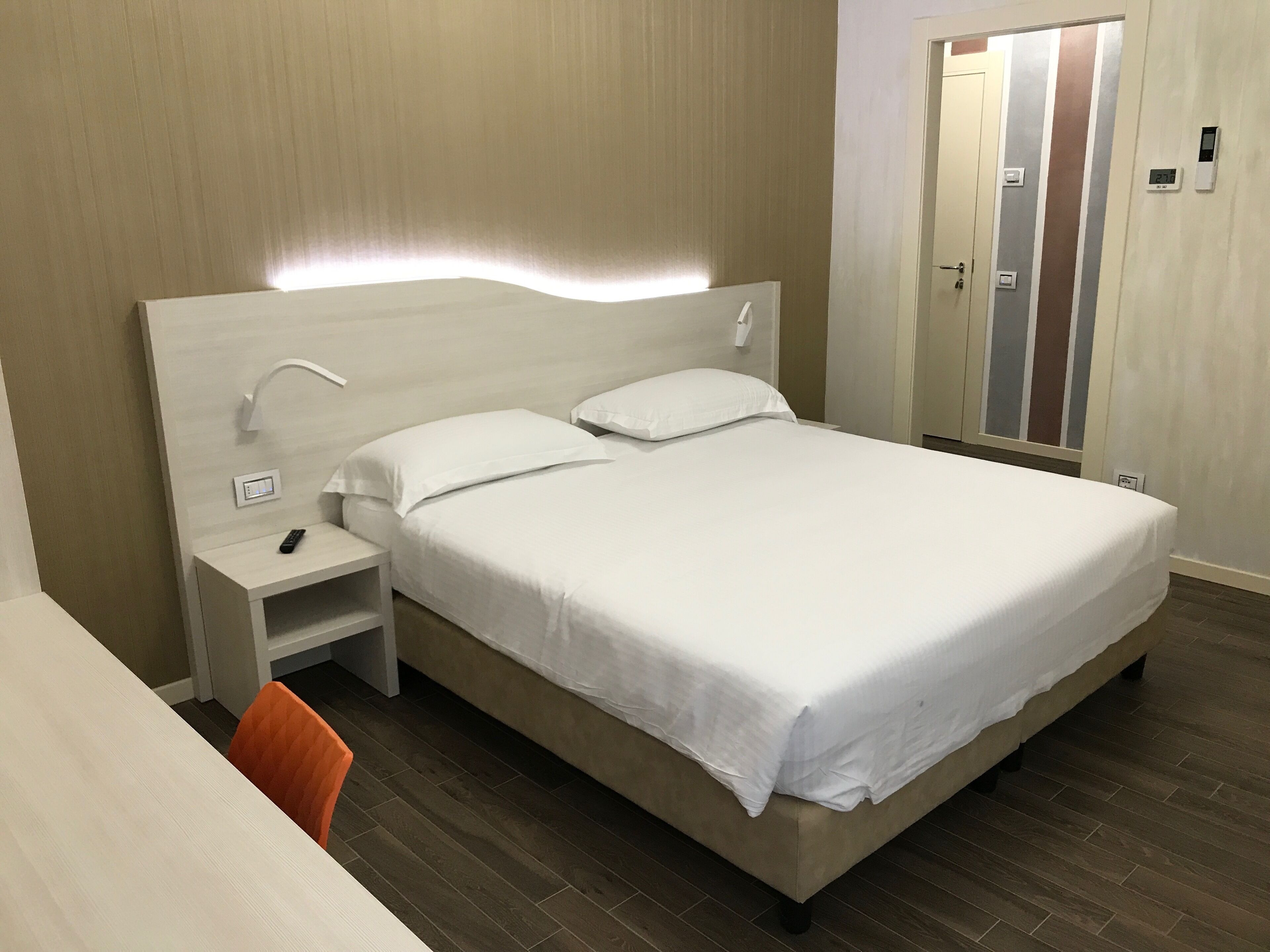 A neatly arranged hotel room with a bed, bedside table, and a chair.