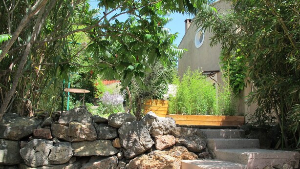 A stone staircase leading up to a building with a circular window, surrounded by lush greenery and a wooden planter. - Charming gîte for 5 people with private heated swimming pool in St Maximin (Saint-Maximin-la-Sainte-Baume)