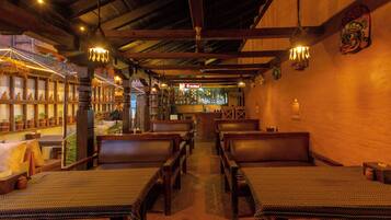 Interior de restaurante com bancos de madeira, luminárias pendentes e área de bar ao fundo.