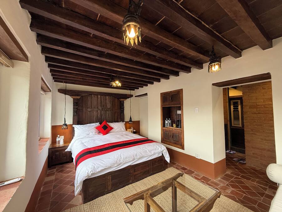 Un dormitorio con una cama de madera, una mesita de noche, una pequeña mesa auxiliar, un estante en la pared con botellas y una puerta que da a otra habitación.