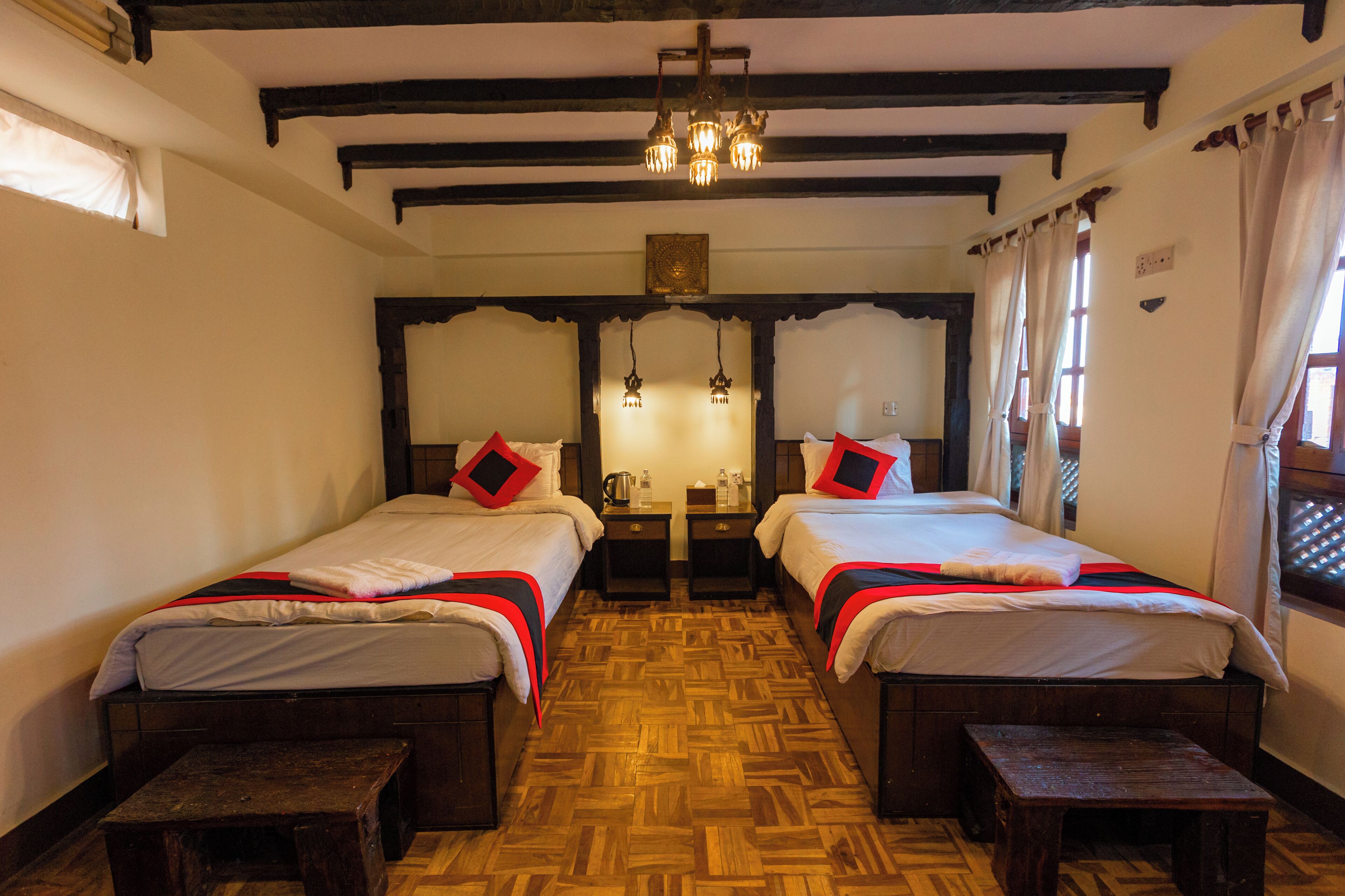 A room with two beds, wooden benches, a wooden floor, a chandelier, and a window with curtains.