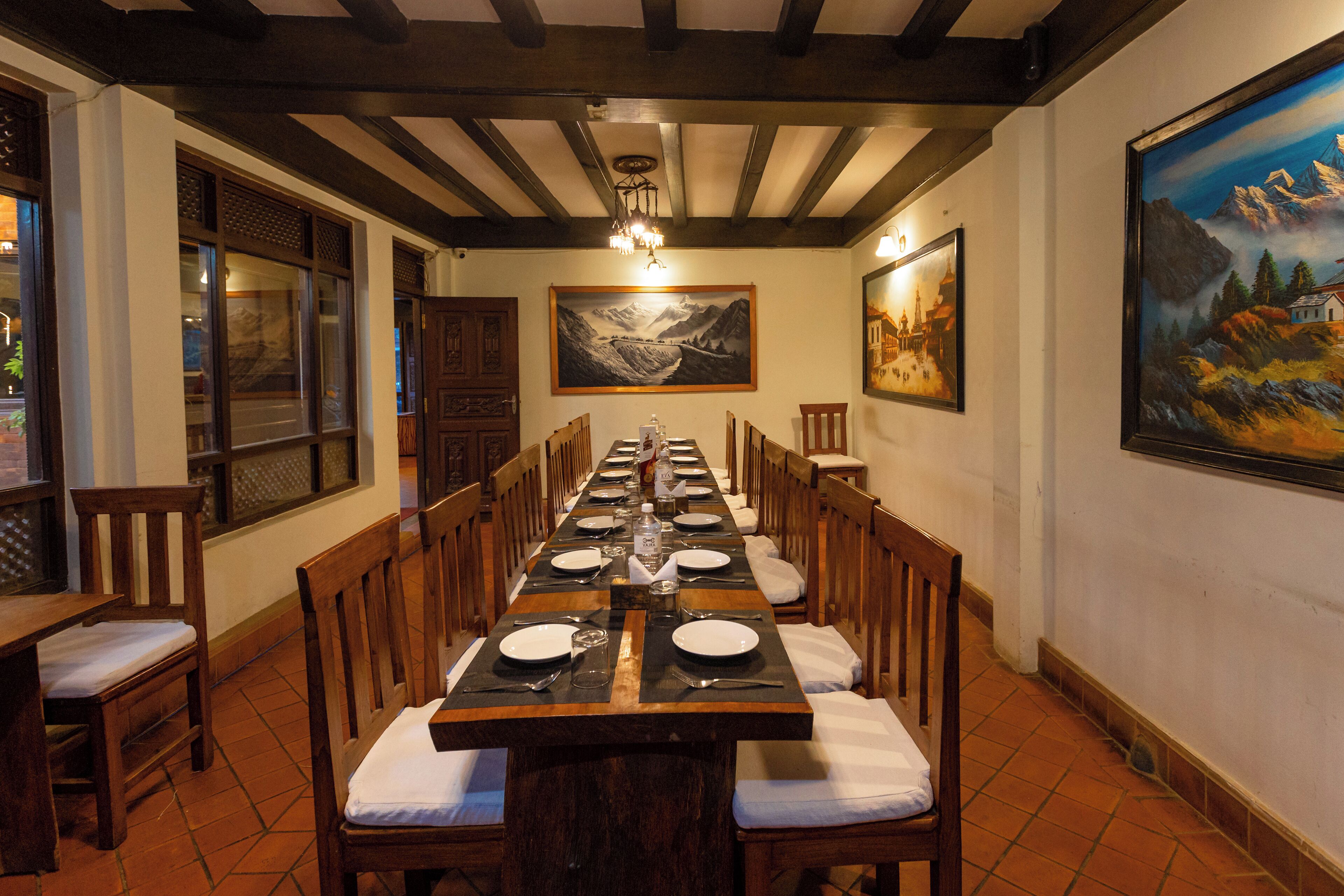 A long dining table set with chairs, a chandelier, and paintings on the walls.