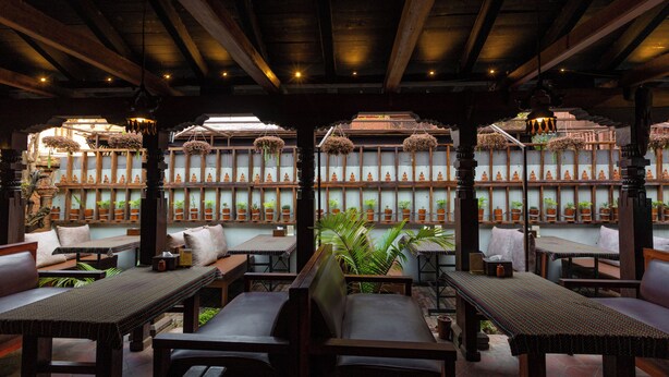 Un espacio interior con mesas y sillas de madera, plantas en macetas y un estilo arquitectónico tradicional.