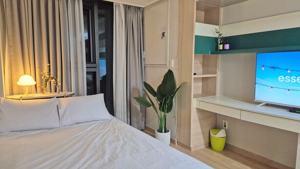 Una habitación de hotel con una cama, un escritorio con televisor, una planta y una lámpara.