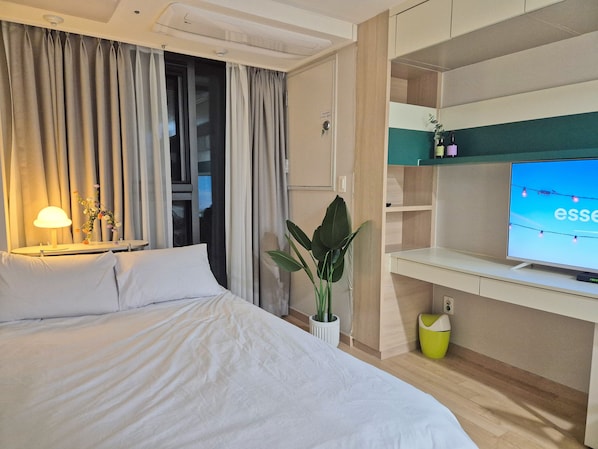 Une chambre d’hôtel avec un lit, un bureau avec une télévision, une plante et une lampe.