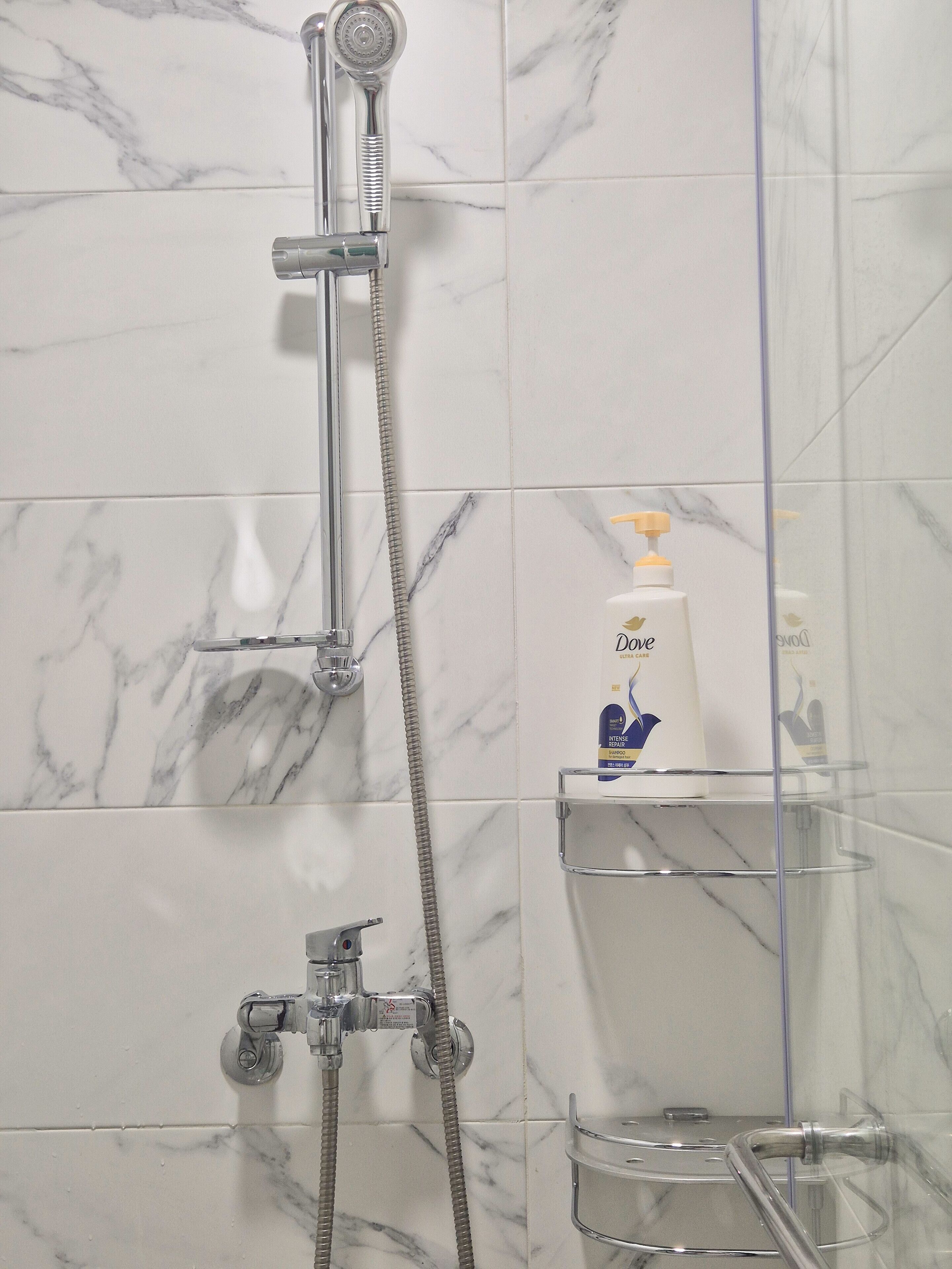 A bathroom with a shower, marble tiles, and a soap dispenser on a shelf.