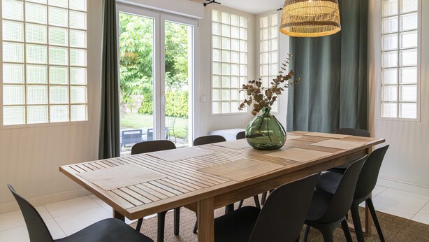 Un comedor con una mesa de madera, sillas negras y un jarrón verde con flores.