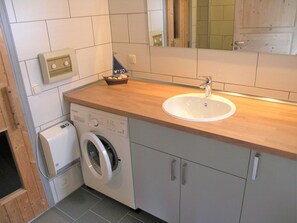 Ein modernes Badezimmer mit Holztresen, Waschbecken, Waschmaschine und Spiegel.