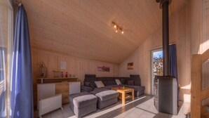 Ein gemütliches Blockhaus-Interieur mit Holzbalkendecke, einer Sofagarnitur, einem kleinen Tisch und einem Kamin.
