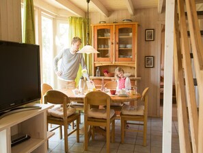 Ein Holzinnenraum mit einem Esstisch, Stühlen, einem Fernseher und einem Schrank.