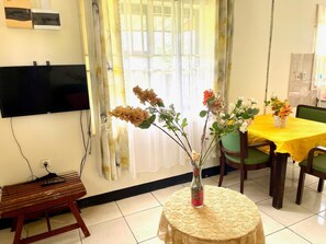 A dining area with a table set for two, a television mounted on the wall, and a small wooden bench. - 3 Bed House - Sleeps 6 - Garden - Parking - Wifi (Paramaribo)