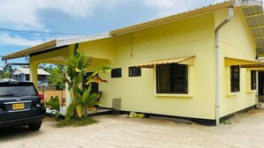 A yellow building with a covered porch, a car parked in front, and a plant near the entrance. - Tropical Paradise in Paramaribo 3 - Room House (Paramaribo)