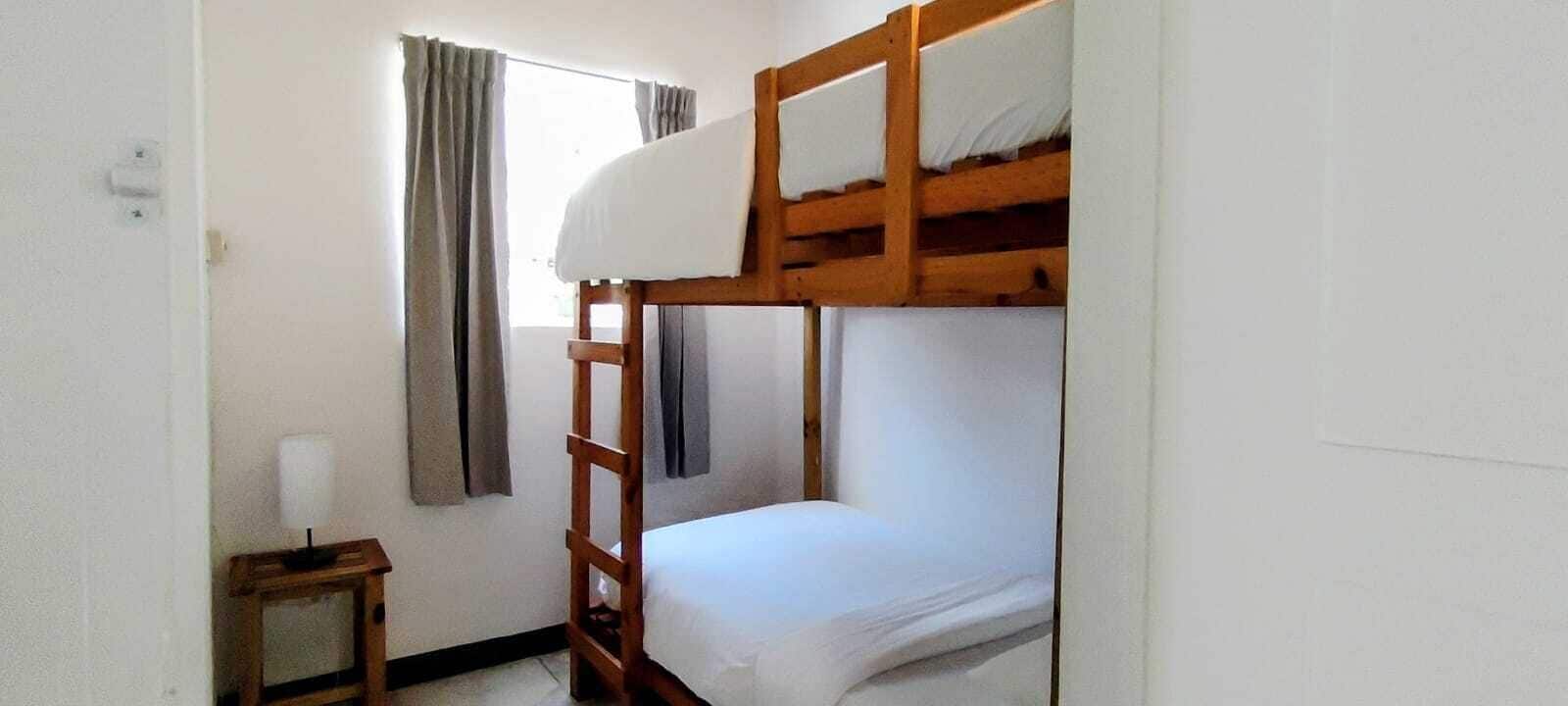 Une chambre avec un lit superposé, une échelle, une petite table avec une lampe et une fenêtre avec des rideaux.