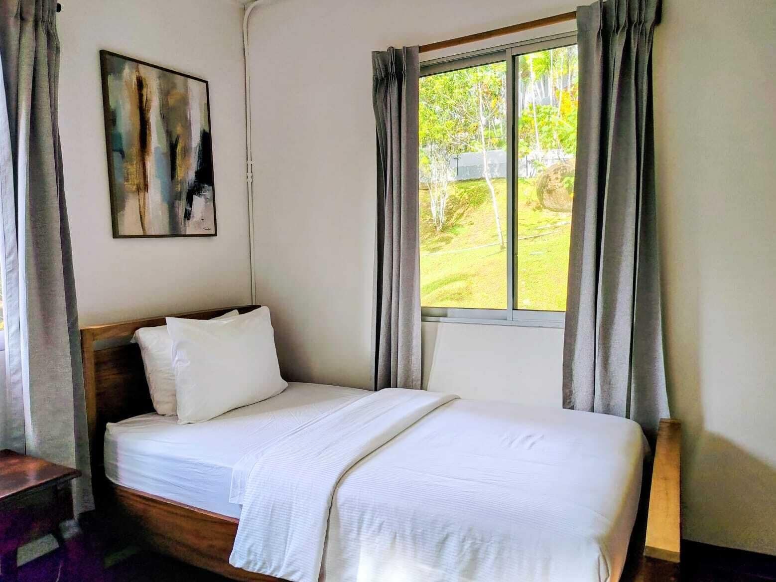 Una cama con cabecera de madera, un cuadro en la pared y una ventana con cortinas.