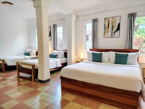 Habitación de hotel con dos camas individuales, una cama grande, piso a cuadros y una ventana con cortinas.