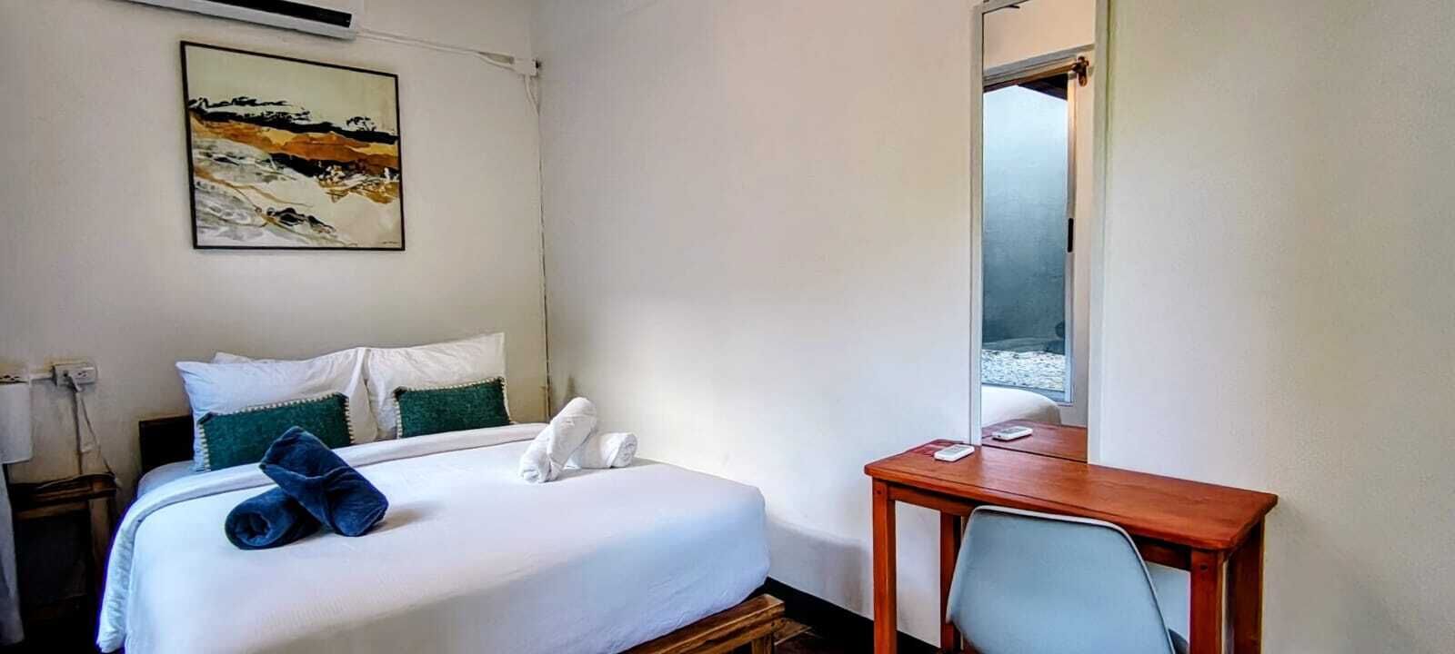 Habitación de hotel con cama, escritorio, una silla, un cuadro en la pared y una ventana.