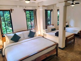 Habitación de hotel con dos camas, ventanas amplias, ventilador de techo y vista a zonas verdes.