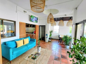 A room with a blue sofa, a television, wicker hanging lights, and potted plants. - Alma Vida Hotel (Quepos)