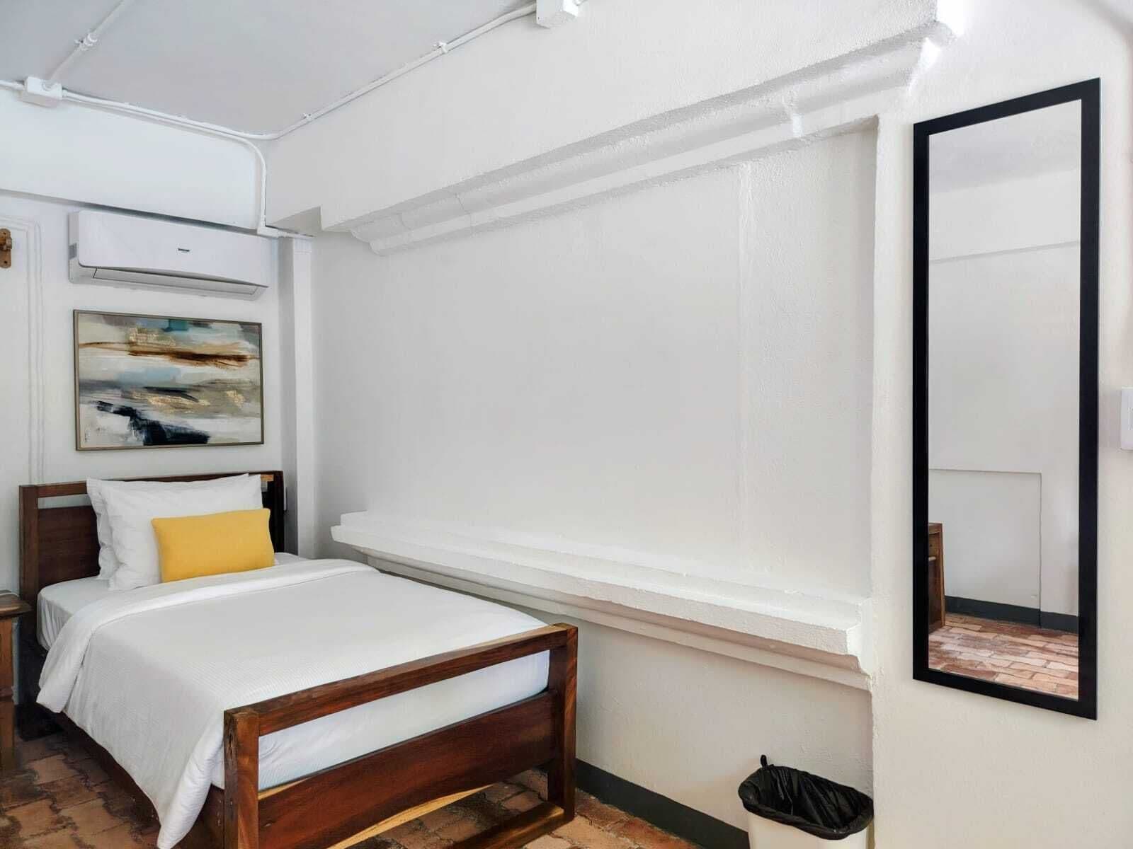 Um quarto com cama, janela, ar condicionado fixado na parede e um quadro.