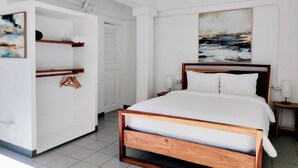 Ein Schlafzimmer mit einem hölzernen Bett, weißen Wänden, einem Gemälde und einem Kleiderschrank mit Kleiderbügeln.