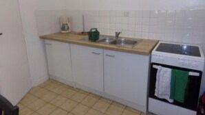 A small kitchen with white cabinets, a wooden countertop, a sink, a stove, and a green kettle. - Le Goéland - Dieppe (Dieppe)