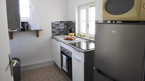 A compact kitchen with a built-in microwave, a stainless steel refrigerator, a window, and a tiled backsplash.
