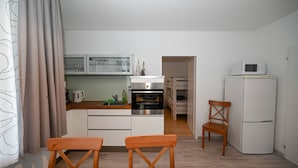 A compact kitchen with white cabinets, a microwave, and a refrigerator. There are two wooden chairs and a small table in the foreground. - Domizil Alpine Retreat 11 with balcony (Kaprun)