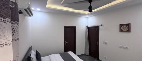 Una habitación de hotel moderna con una cama bien hecha, un ventilador de techo y un equipo de aire acondicionado.
