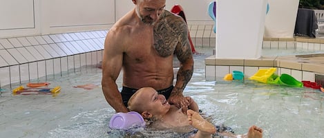 A man in a swimming pool with a child, surrounded by various pool toys.