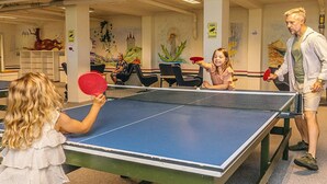 Een tafeltennistafel in een kamer met stoelen en een muurschildering.