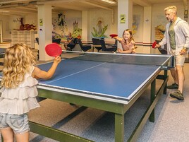 Et bordtennisbord i et rum med stole og et vægmaleri.