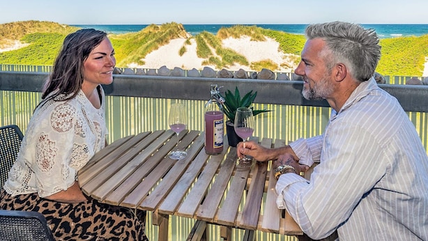 Een stel zit aan een houten tafel met uitzicht op het strand en de duinen.