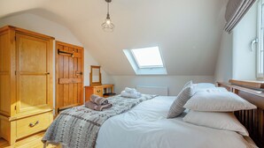 A bedroom with a sloped ceiling, a skylight, a wooden wardrobe, a bedside table, and a bed with white bedding. - 2 bedroom accommodation in Chwilog, near Pwllheli (Chwilog, near Pwllheli)