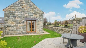 A stone cottage with a wooden door, a small patio with a table and chairs, and a stone wall in the background. - 2 bedroom accommodation in Chwilog, near Pwllheli (Chwilog, near Pwllheli)